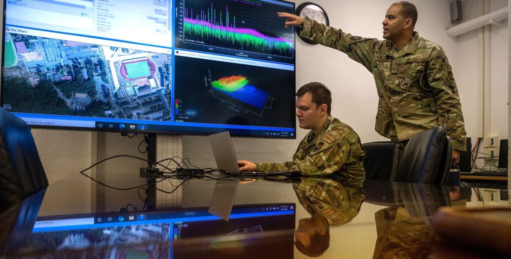 USAF techs discuss electromagnetic spectrum operations at computer monitors.