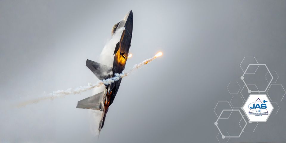 An F-22 Raptor with its nose point up to the gray sky with defensive flares released