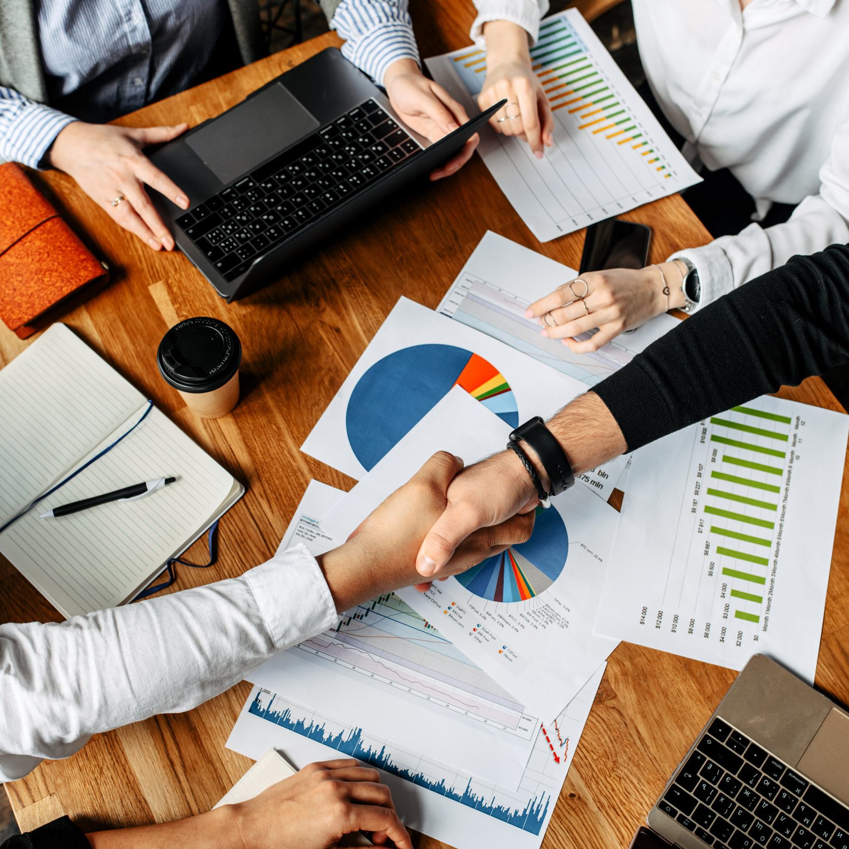 The result of a successful meeting. Top view of men shaking hands above papers with graphs and diagrams, their faces are not visible