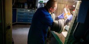 materials chemist works in a glove box, preparing a container filled with bead bits that will turn brown if someone attempts to tamper with the container’s contents