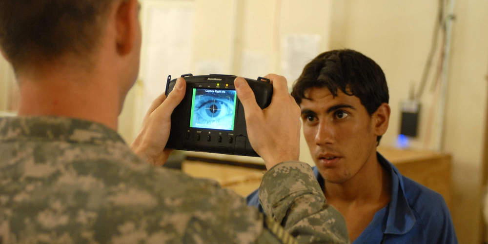 US Army soldier uses a biometrics camera to capture iris biometrics data on workers at a forward operating base in northern Baghdad.