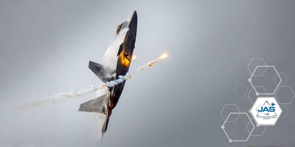 An F-22 Raptor with its nose point up to the gray sky with defensive flares released