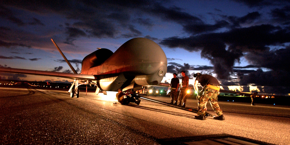 Image of several Department of Defense personnel inspecting an unmanned aircraft on a runway.