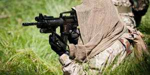 Servicemember with cloth covering over head aiming weapon system.