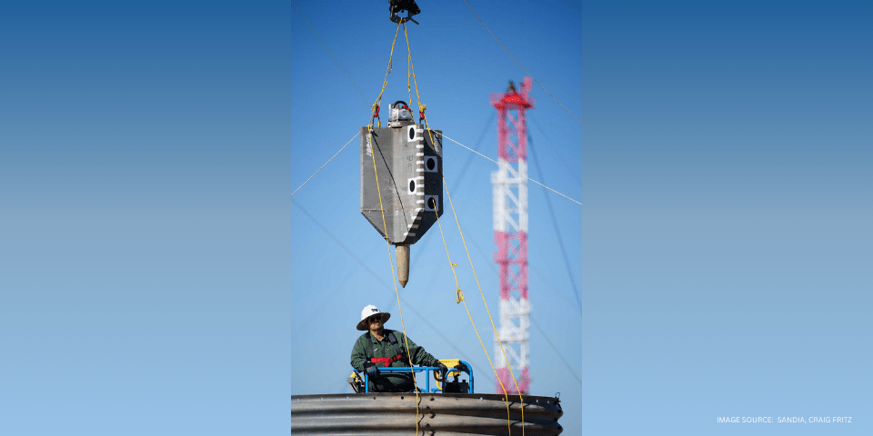 Technologist Jamie Meza guides a torpedo anchor prototype as it is lifted over a test bed at the Drop Tower facility. The anchor is being tested for use with offshore wind turbines. (Photo by Craig Fritz)